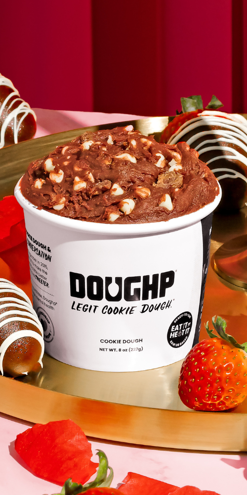 hand reaching into plate full of red velvet cookie dough bites with cupcake nearby and Doughp's cookie dough drops bag behind