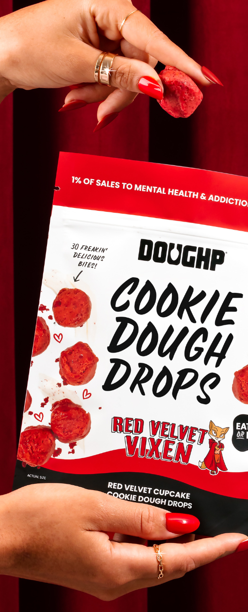 hand reaching out of the cookie dough drops bag with one red velvet cookie dough drop in her hands